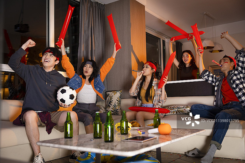 快乐的年轻人在客厅观看足球比赛:欢呼呐喊庆祝胜利图片素材