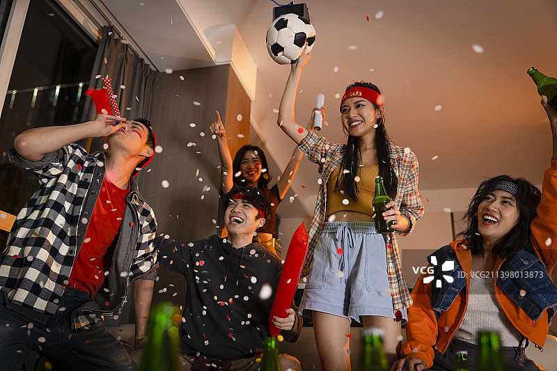 快乐的年轻人在客厅观看足球比赛:欢呼呐喊庆祝胜利图片素材