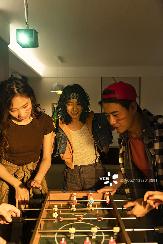 快乐的年轻人在客厅玩桌上足球图片素材