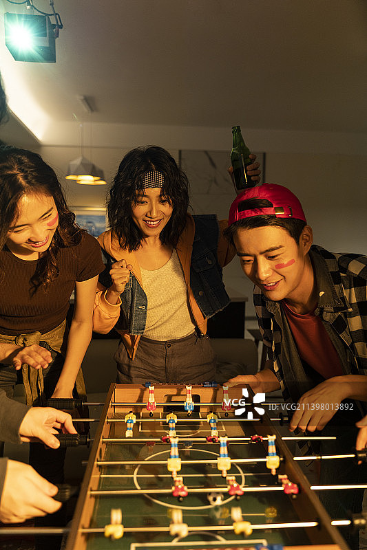 快乐的年轻人在客厅玩桌上足球图片素材