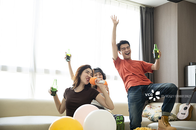 年轻朋友在家聚会唱卡拉OK、喝啤酒嬉戏玩耍图片素材
