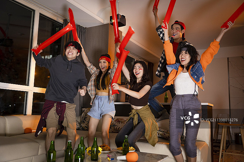 快乐的年轻人在客厅观看足球比赛:欢呼呐喊庆祝胜利图片素材