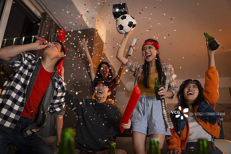 快乐的年轻人在客厅观看足球比赛:欢呼呐喊庆祝胜利图片素材