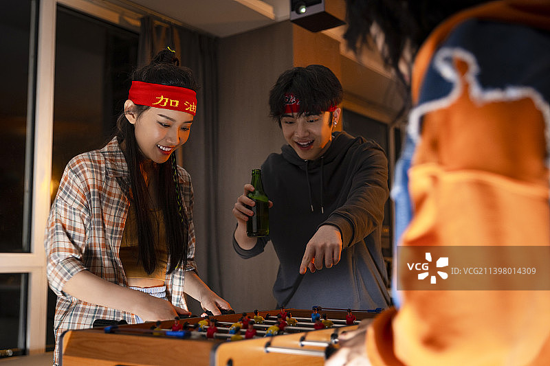 快乐的年轻人在客厅玩桌上足球图片素材