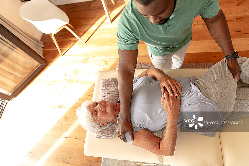 非裔美国男理疗师在家为白人老年妇女进行按摩治疗图片素材