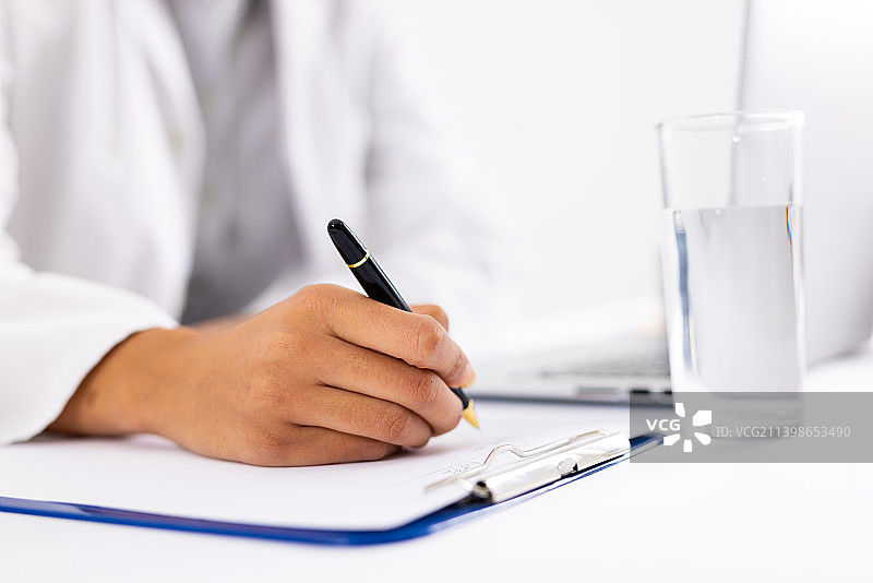 非洲裔美国中年女医生在写字板上书写，旁边有水杯和笔记本电脑图片素材