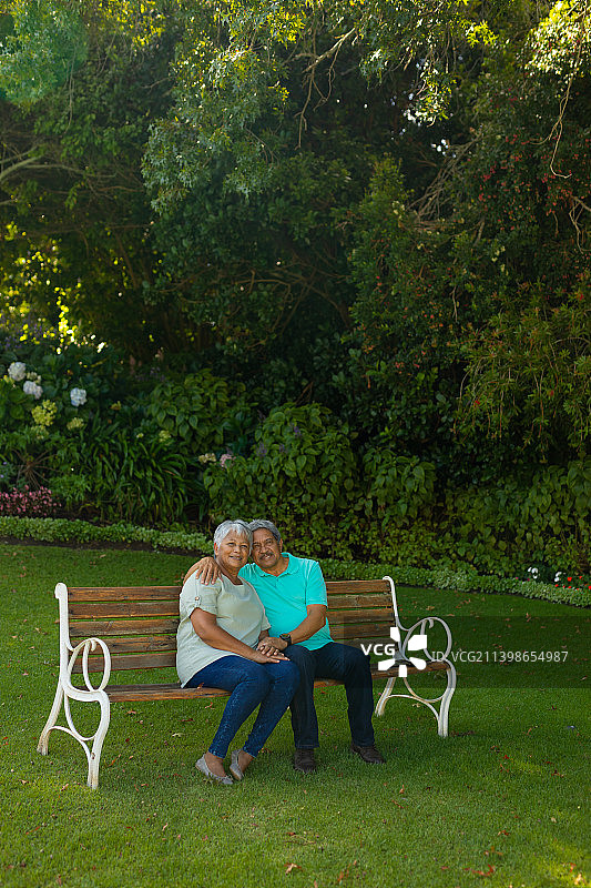 微笑的黑白老年男子的肖像与妻子坐在长椅上对树木和植物在公园图片素材
