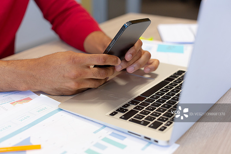 西班牙裔男性顾问在会议室用智能手机和笔记本电脑的半身照图片素材