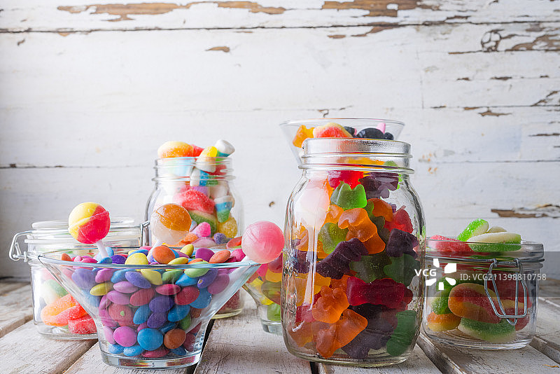 木桌上罐子和碗里各种彩色糖果和棒棒糖特写图片素材