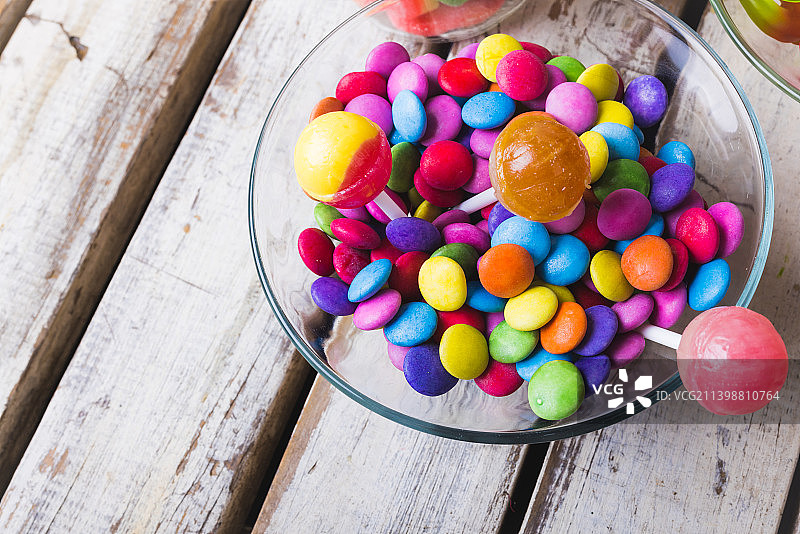 白色木桌上玻璃碗中彩色棒棒糖和巧克力糖果的高角度视图图片素材