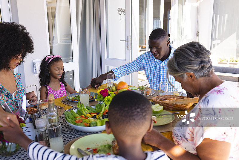 在餐桌上，多代同堂的多种族家庭在午餐前手牵着手祈祷图片素材