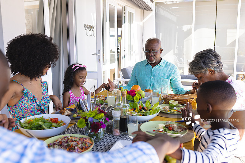 多种族多代同堂家庭在午餐前牵手在餐桌旁祈祷图片素材