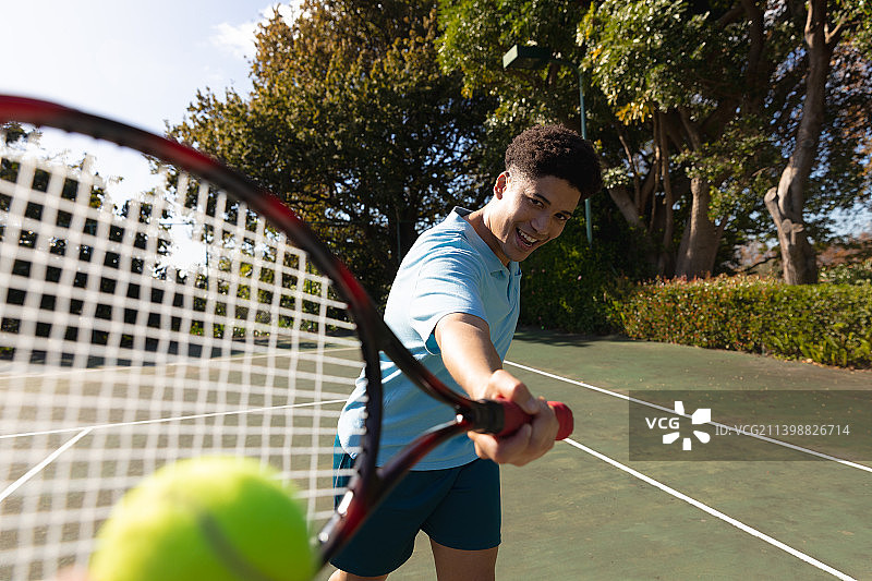 在阳光明媚的户外网球场上打网球的混血男人图片素材