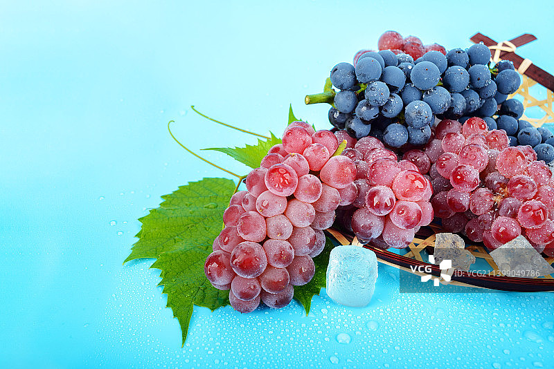 蓝色背景下竹筐里的葡萄冰块图片素材