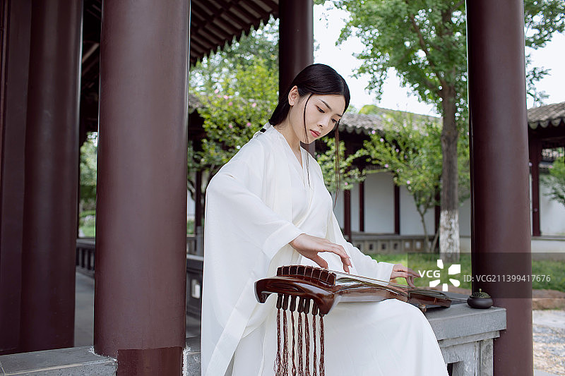 一个古典美女坐在中式园林里弹古琴图片素材