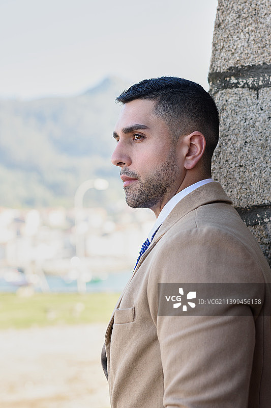 年轻男人靠墙站立，看向远方图片素材