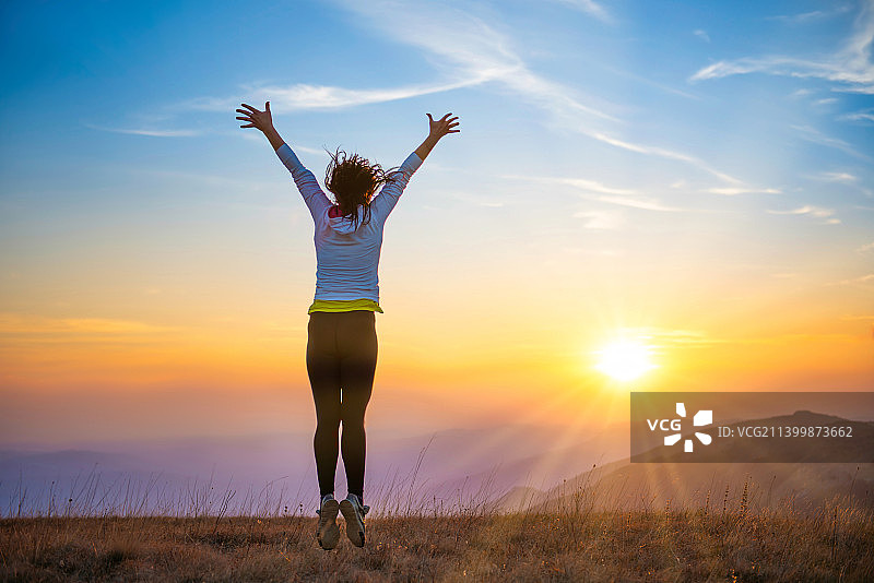 日落时分站在田野上举起双臂的女子背影图片素材