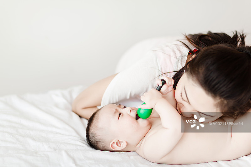 东方年轻妈妈亲吻躺在床上玩耍的儿子图片素材