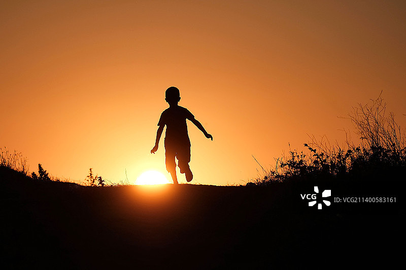 日落时分，田野上行走男孩的剪影图片素材