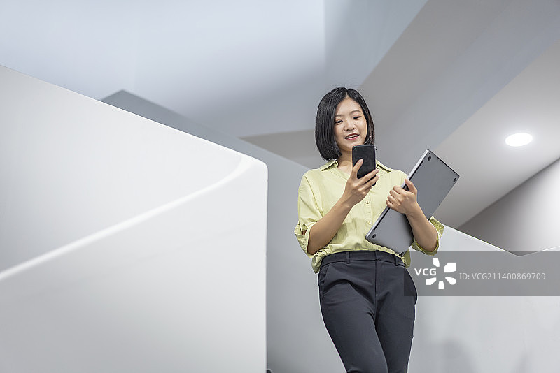 楼梯间拿着笔记本电脑使用手机办公的商务女性特写图片素材