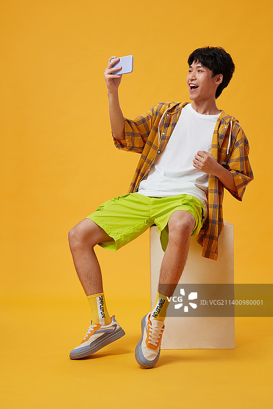 坐在木箱子上玩手机的年轻男孩图片素材