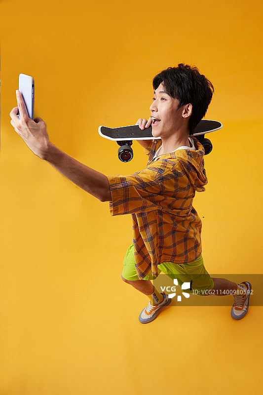 手拿滑板玩手机的年轻男孩图片素材