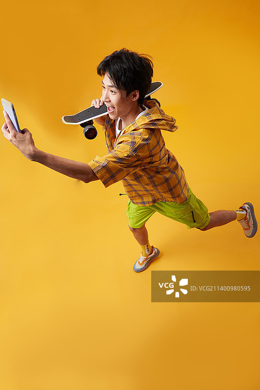手拿滑板玩手机的年轻男孩图片素材