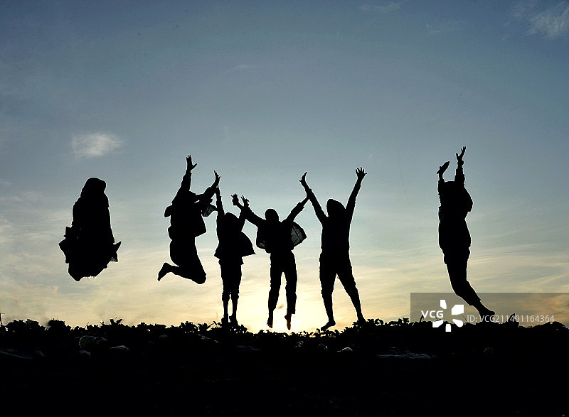 日落时分，朋友们在田野上对着天空跳跃的剪影图片素材