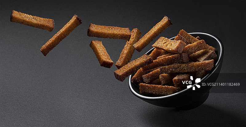 黑色背景上掉落的黑麦面包丁图片素材