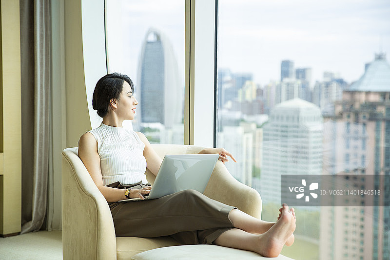 女商人在酒店房间使用笔记本电脑工作、看窗外风景图片素材