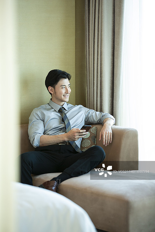 商务男子在酒店房间拿着手机，看窗外风景图片素材
