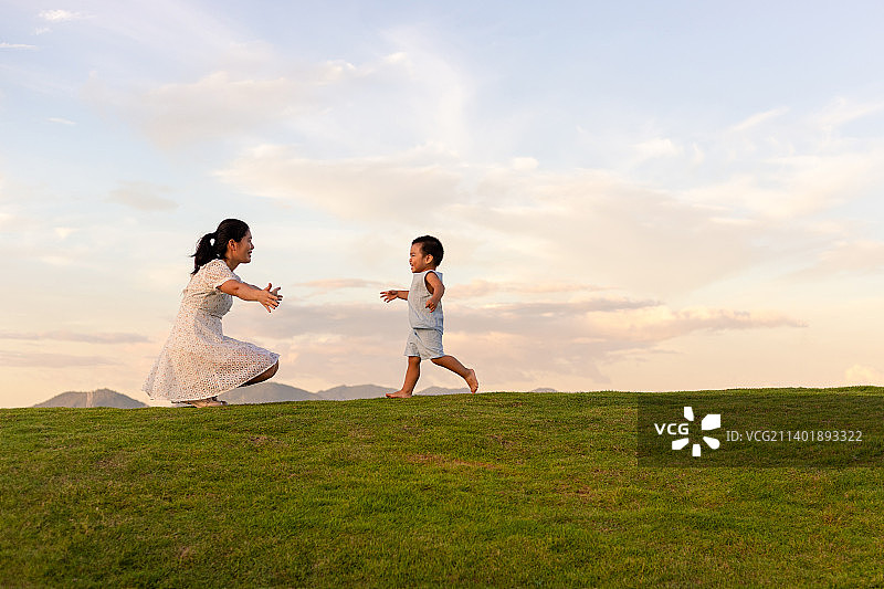 黄昏草地上一个小孩子跑向妈妈怀里图片素材