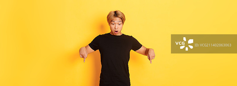 惊讶的亚洲男子张着嘴的肖像，用手指指向图片素材