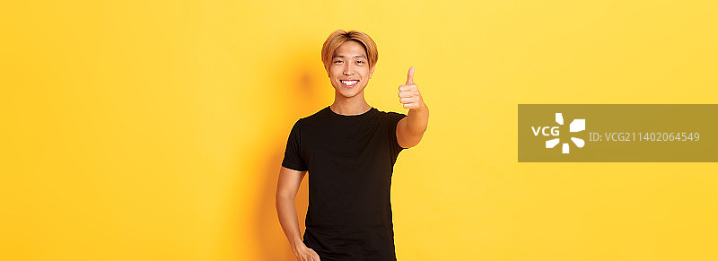 站在黄色背景下的金发满意亚洲男子肖像图片素材