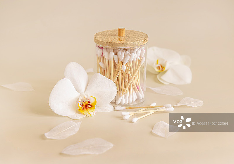 米色背景下，罐子里的竹棉签和白色兰花，环保型护肤品图片素材