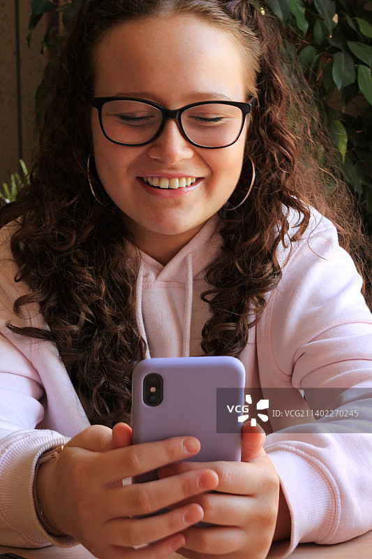 在瑞典斯德哥尔摩，坐在桌旁使用手机的微笑女孩图片素材