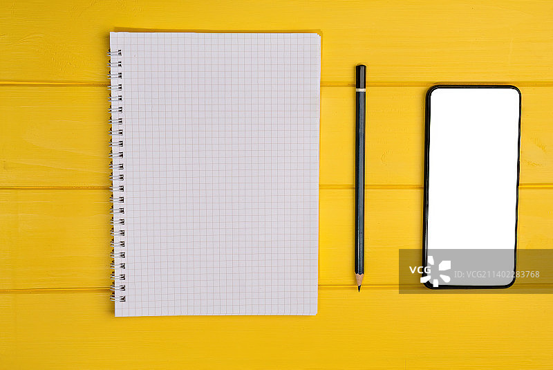 黄色背景上的笔记本和空白智能手机俯视图图片素材