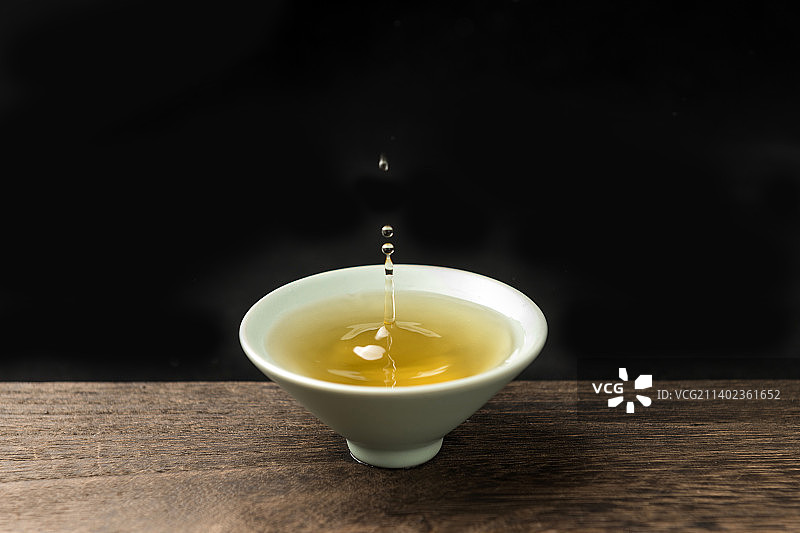 茶水滴落到茶杯中特写木桌面黑色背景图片素材