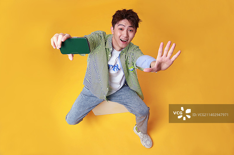 坐在凳子上使用手机的年轻男孩图片素材