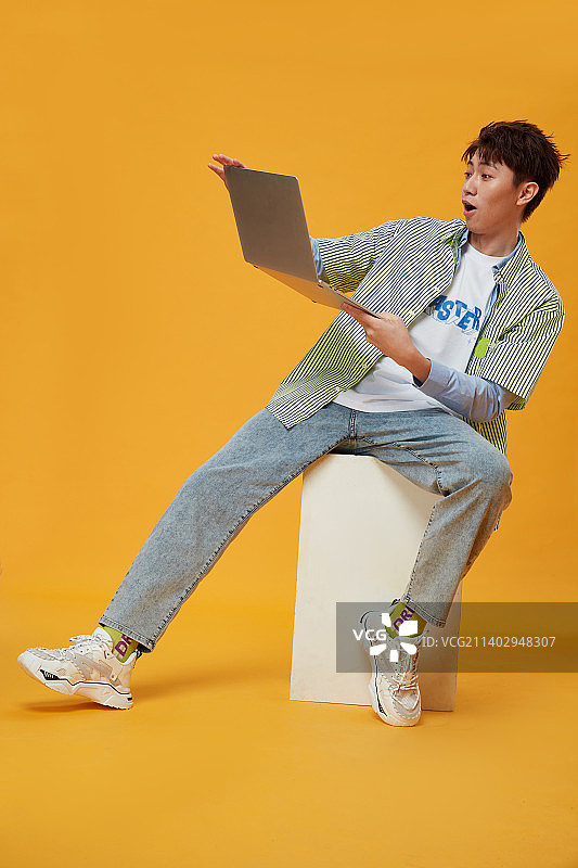 坐在凳子上使用笔记本的年轻男生图片素材