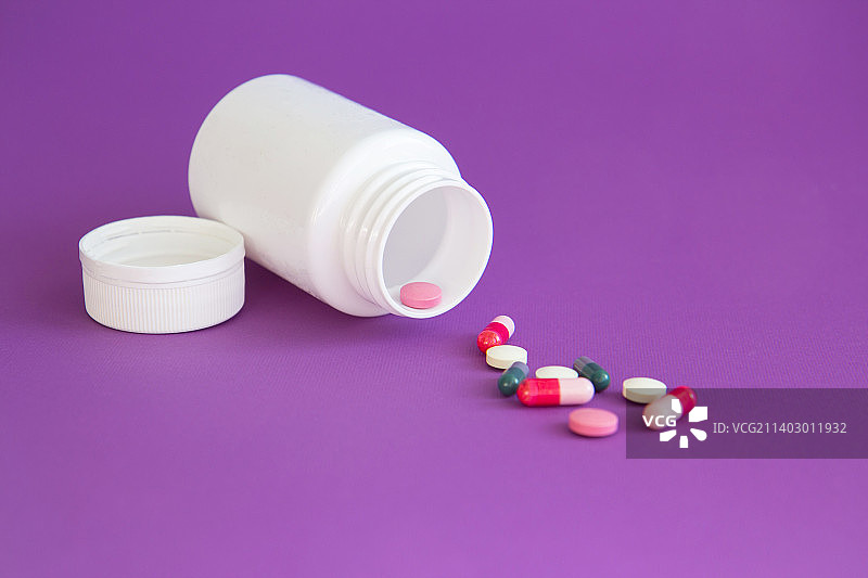 紫色背景上的维生素片剂和胶囊白色瓶子图片素材