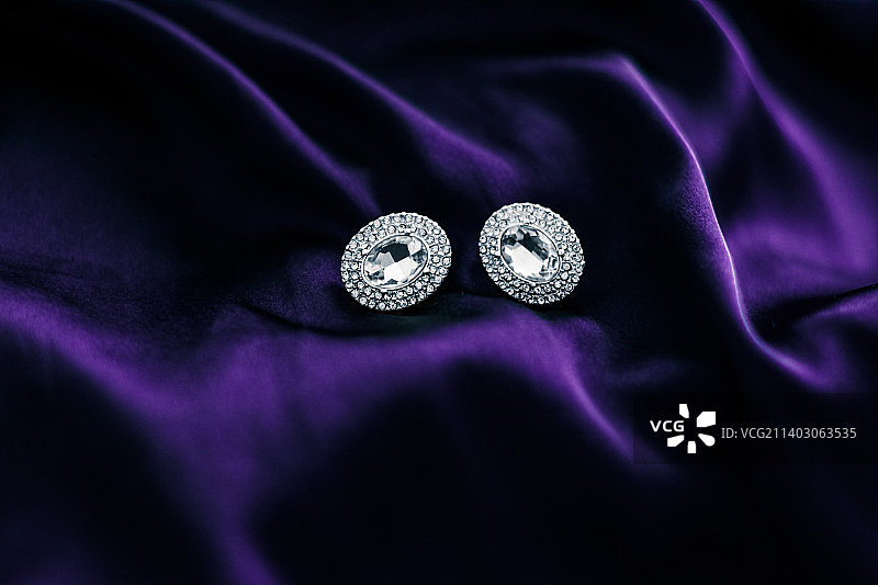 深紫色丝绸面料上的奢华钻石耳环，节日魅力图片素材
