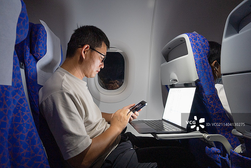 男人在飞机上使用手机和笔记本电脑工作图片素材