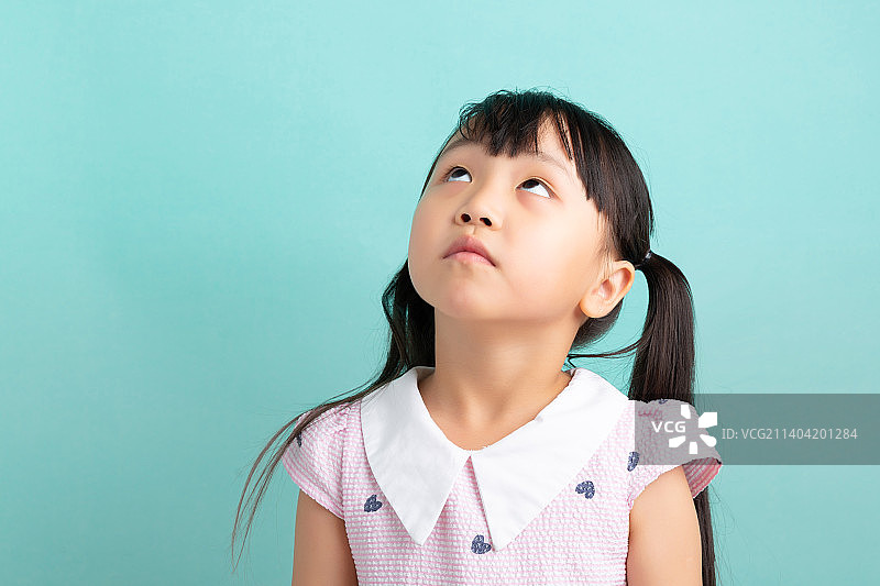 浅蓝色背景前的亚洲小女孩抬头向上看图片素材