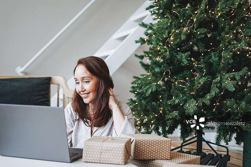 在客厅里用笔记本电脑的年轻女人，旁边有圣诞树图片素材
