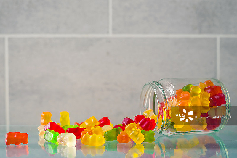 从玻璃罐中洒落在桌子上的彩色糖果特写图片素材
