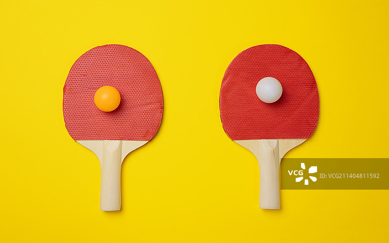 黄色背景上的一对乒乓球木制网球拍图片素材