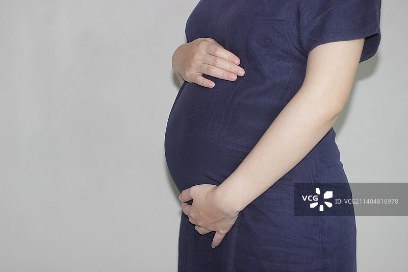 孕妇站在灰色背景前的腰部特写，印度尼西亚万隆图片素材