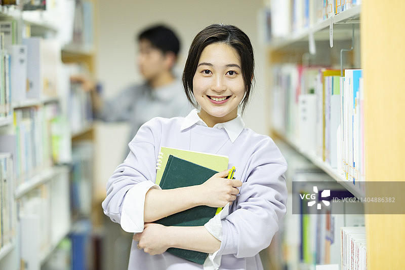 微笑的女学生在图书馆拿着一本书图片素材