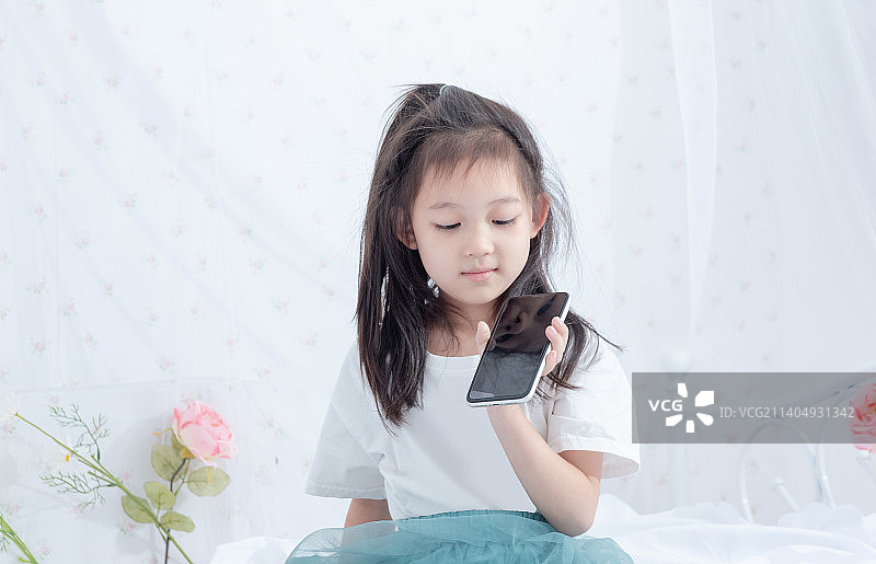 坐在床上拿着手机展示的小女孩图片素材